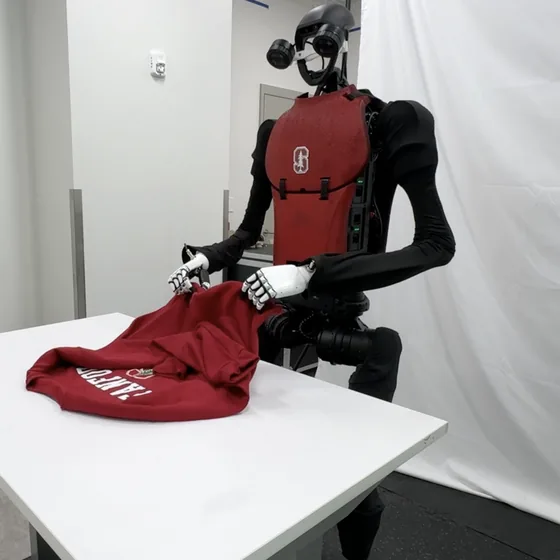 A humanoid robot folding a sweatshirt on a table